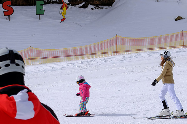Skilehrerin hinter einem Kleinkind fährt die Kinderpiste hinunter